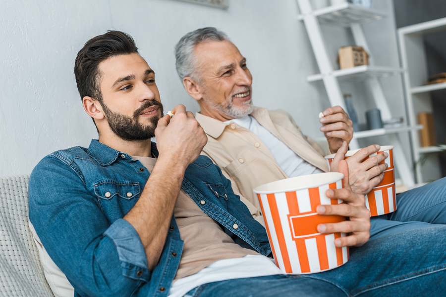 Two men sitting on a couch eating popcorn.