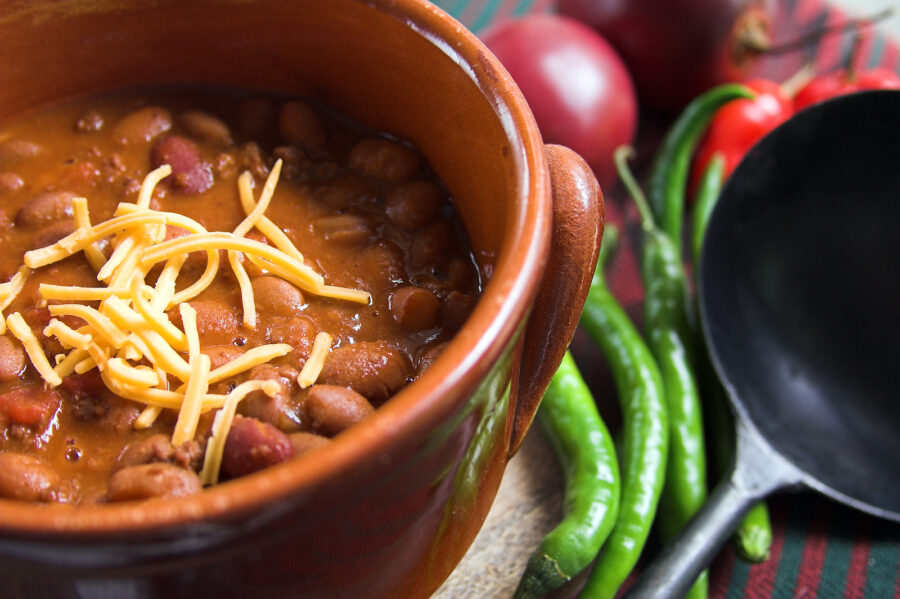 A bowl of chili with cheese and green peppers.