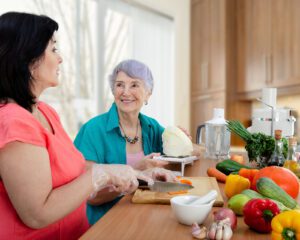 Two women are sitting at a table with vegetables.